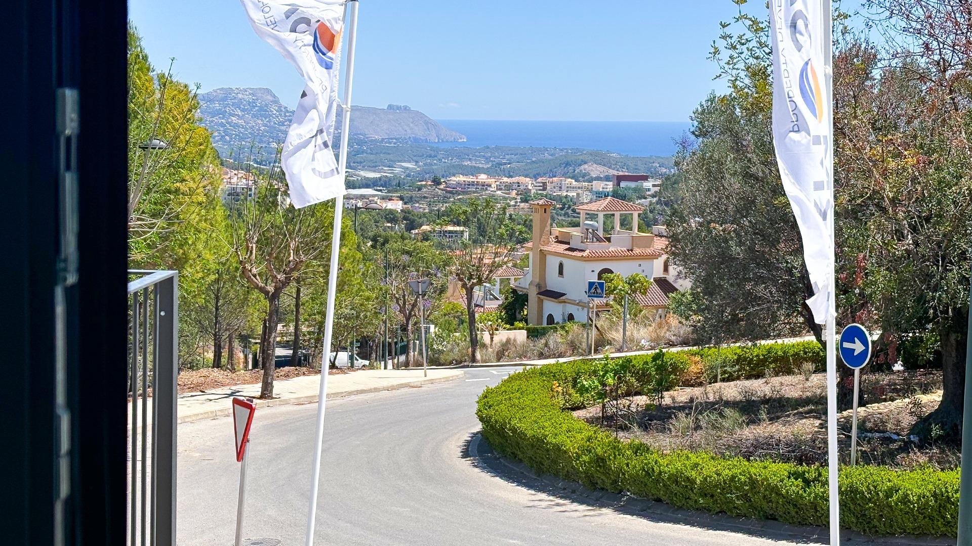 Coastal hillside town with terracotta roofs, a winding road, and the blue sea on the horizon seen beyond trees and houses.