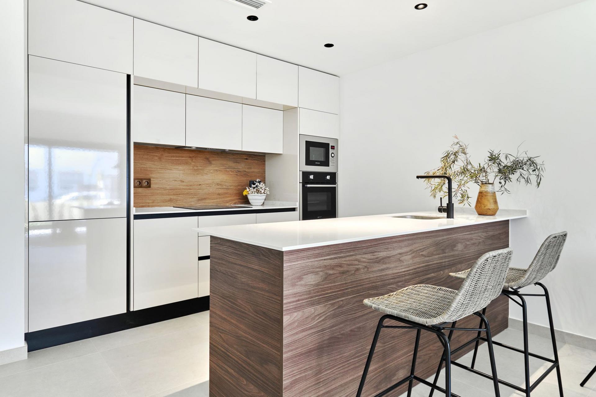 Modern white kitchen with a woodgrain island, built-in oven/mre microwave, and three wicker bar stools at the island.