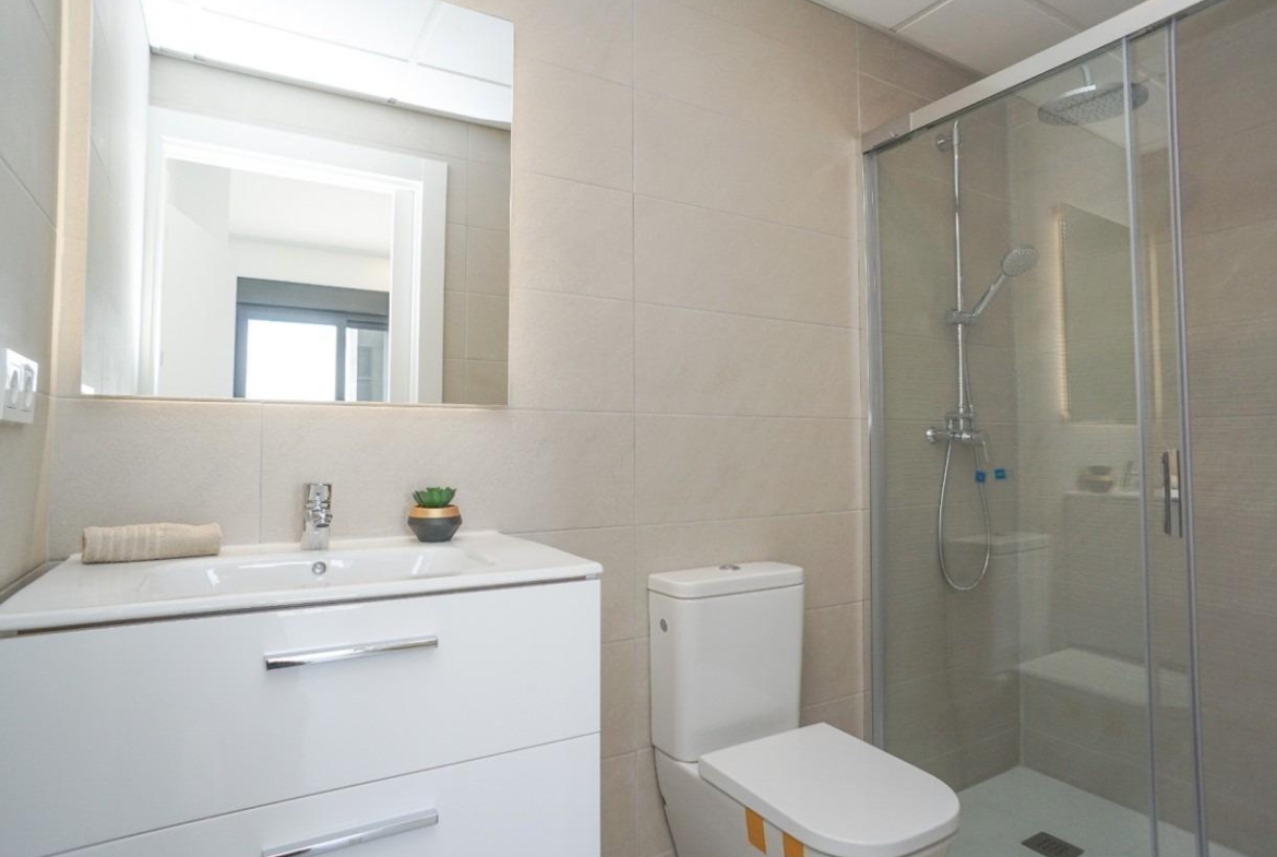 Modern white bathroom with vanity, wall mirror, toilet, and glass shower enclosure.