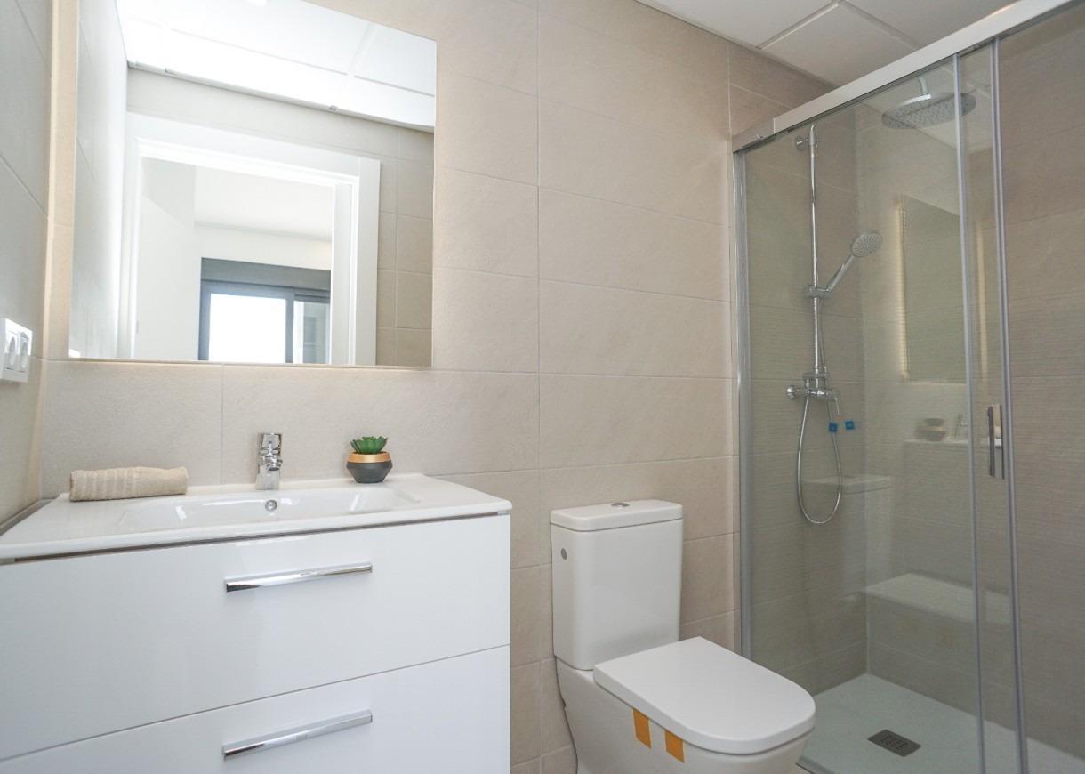 Modern white bathroom with vanity, wall mirror, toilet, and glass shower enclosure.