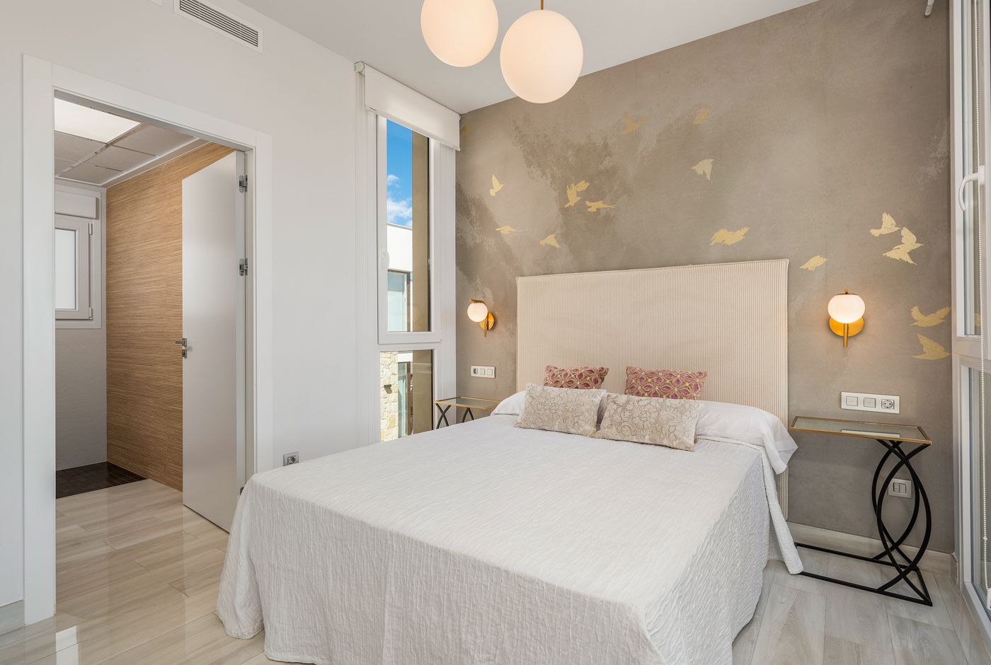 Modern hotel bedroom with a white bed, beige headboard, and a wall mural of golden birds.