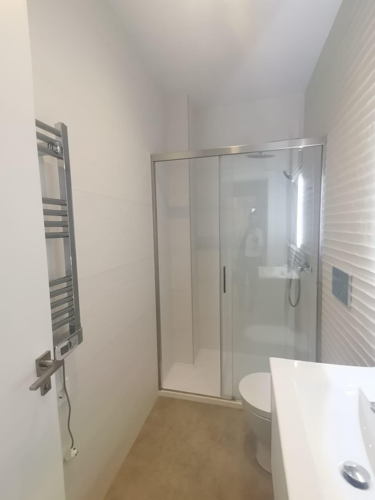 Modern bathroom with a glass-enclosed shower, towel warmer on the left, and a white vanity/sink area on the right.