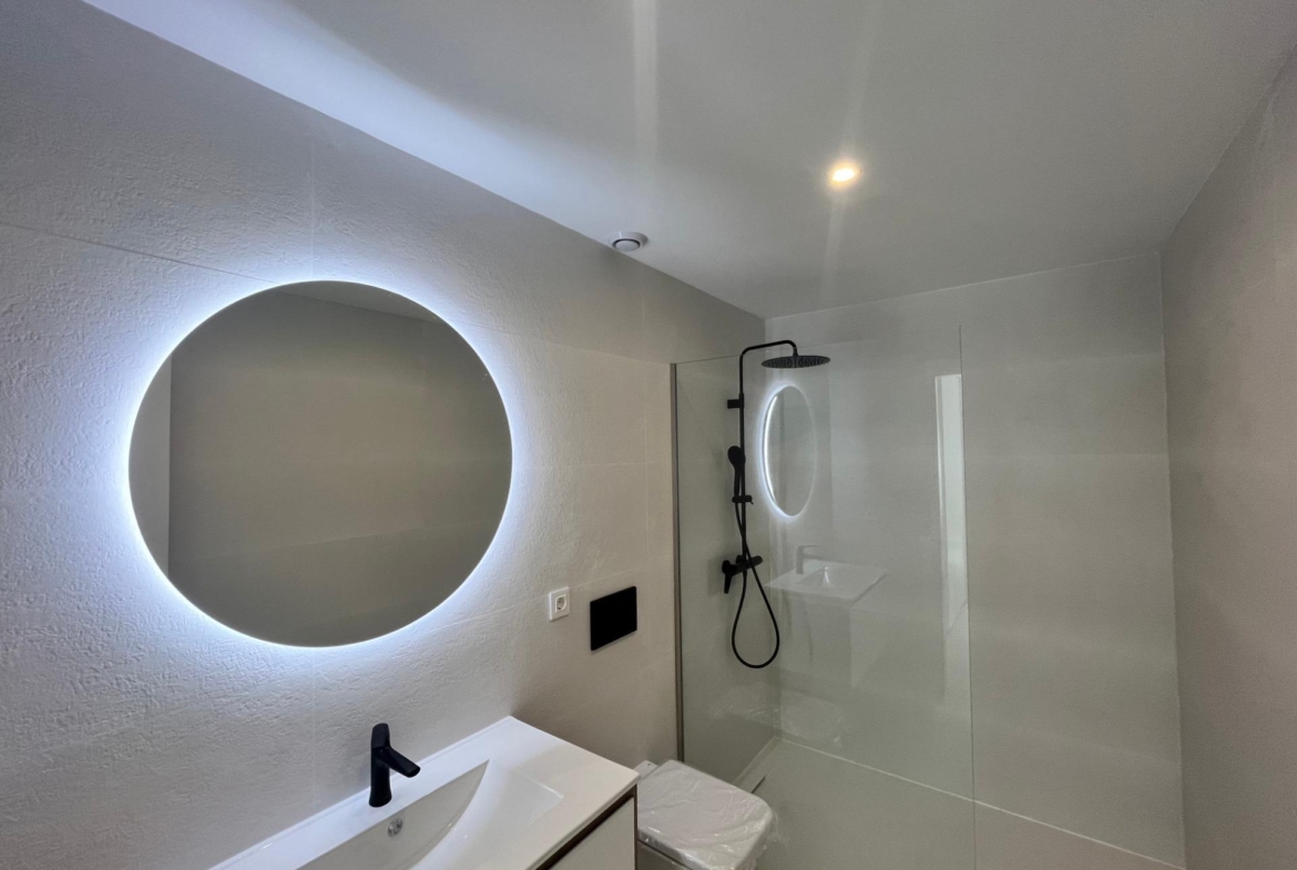 Modern bathroom with a round backlit mirror above a white vanity and a glass shower enclosure.