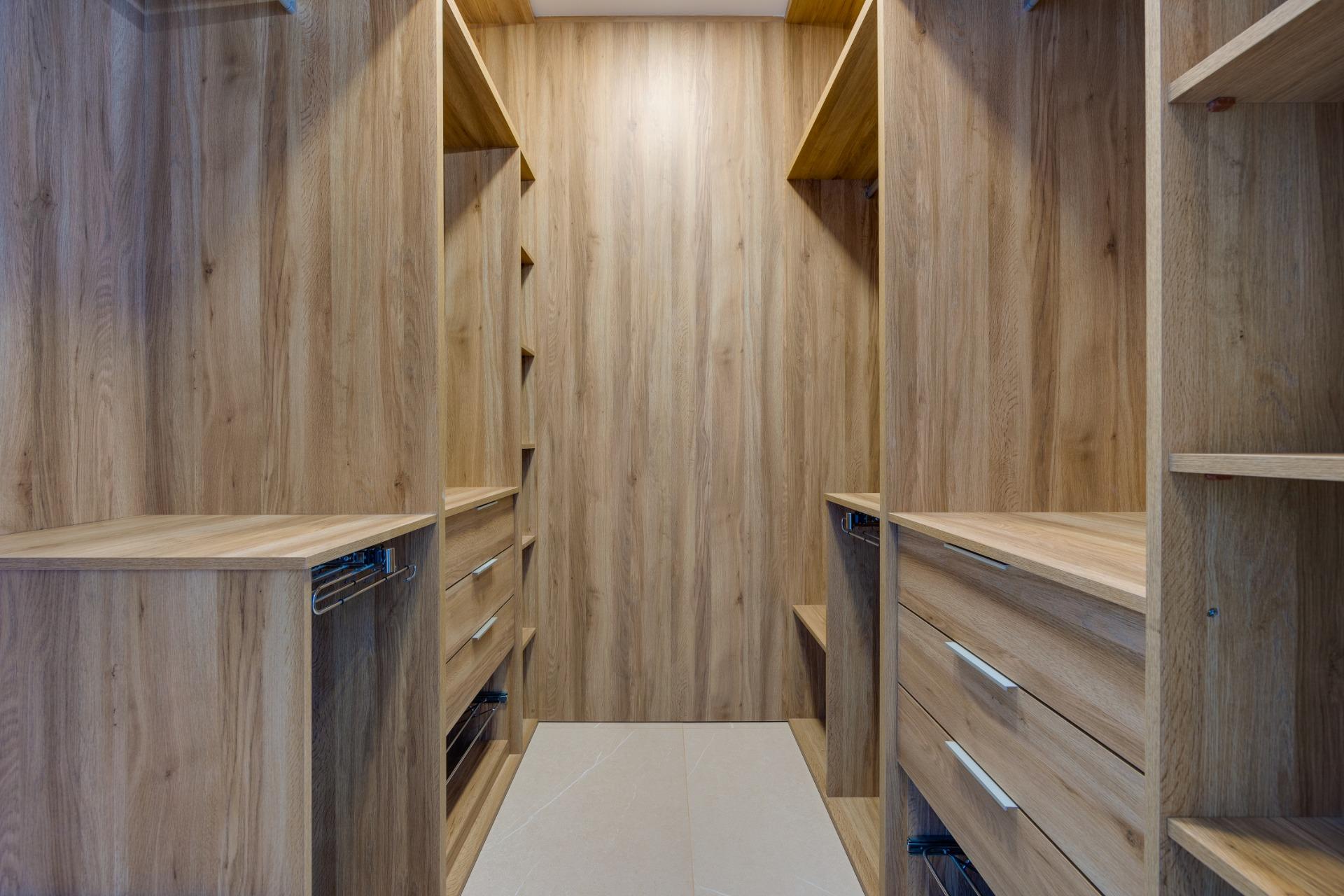 Walk-in wooden closet with tall shelves, drawers, and metal pull-out baskets along the walls, in an oak finish.