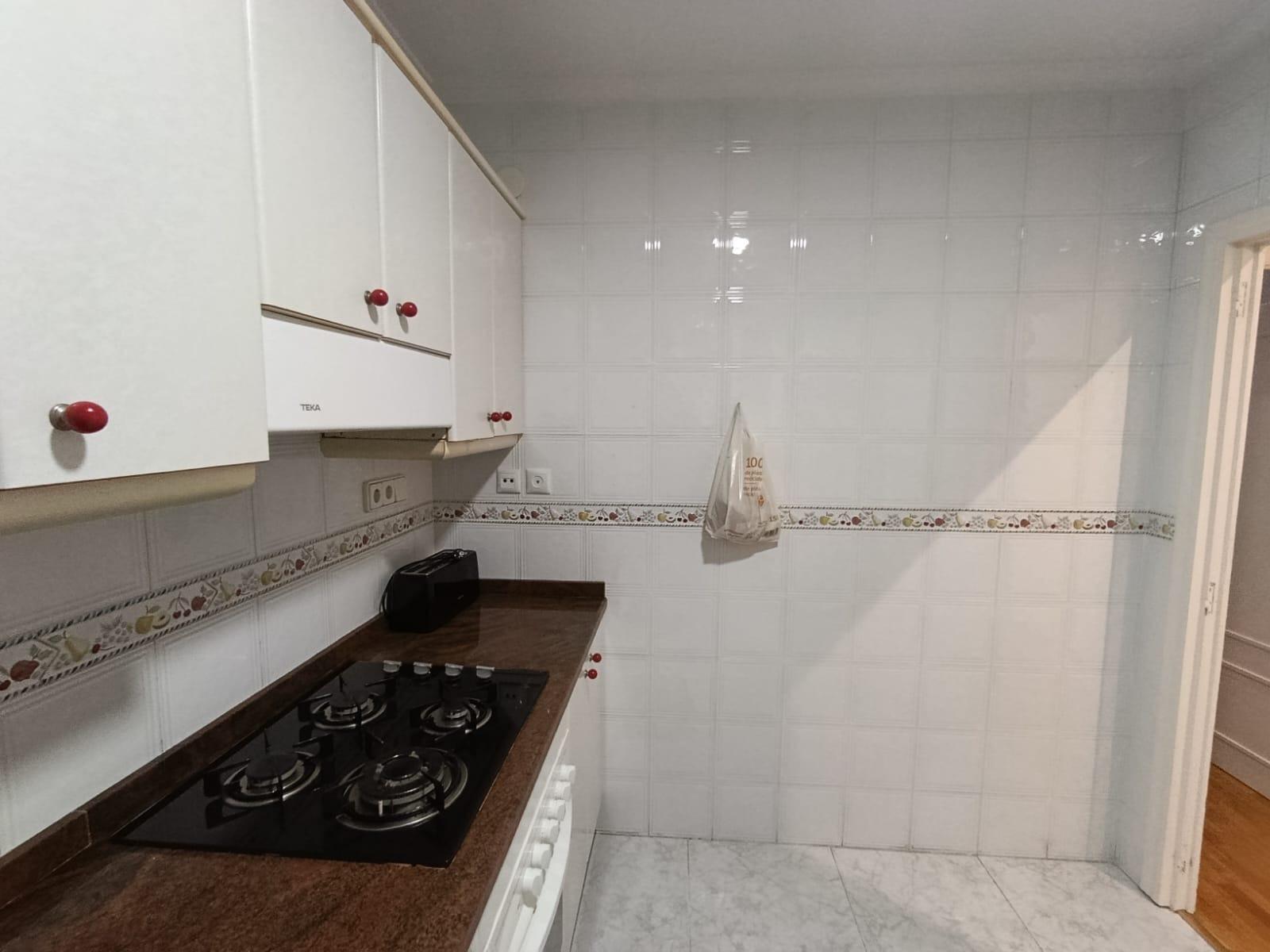 Compact white kitchen with glossy cabinets, red knobs, and a dark brown countertop gas hob. The tiled wall has a decorative border, and a toaster sits on the counter without clutter.