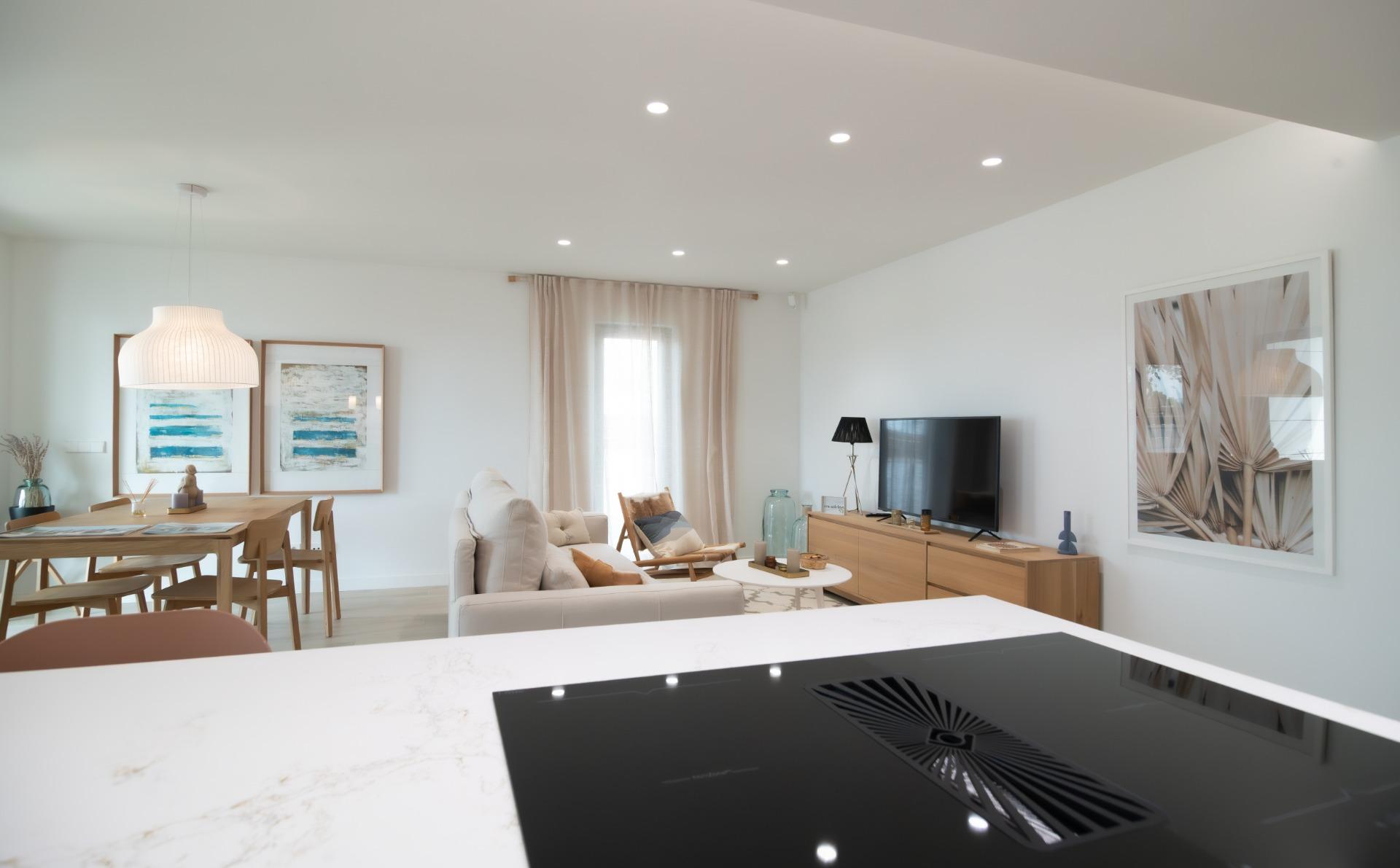 Open-concept living area with beige sofa, wooden dining table, large wall art, TV on a wooden console, and a marble kitchen island in the foreground.