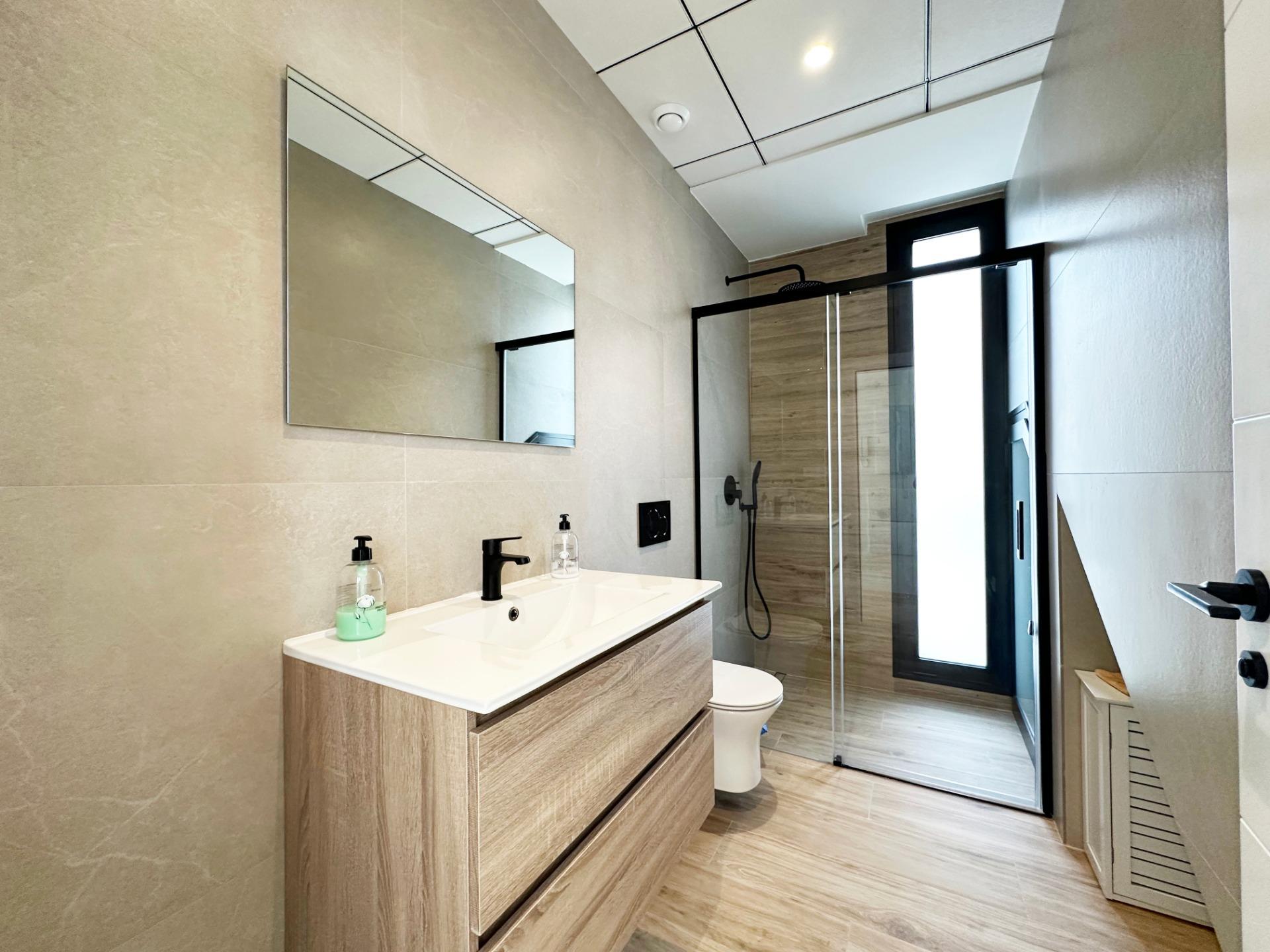 Modern bathroom with a double-sink vanity, large mirror, beige tiled walls, and a glass-enclosed shower.