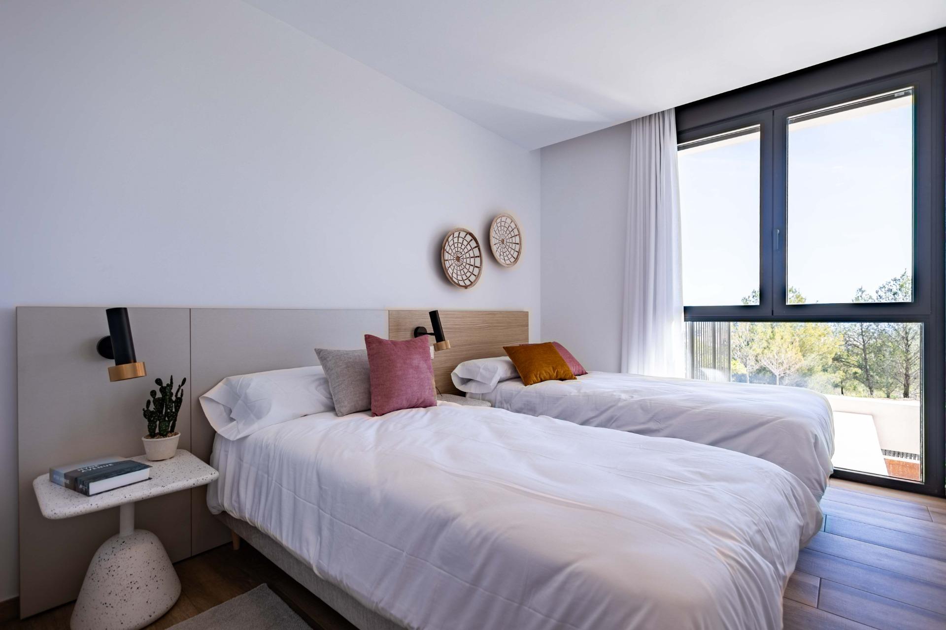 Twin beds in a bright hotel room with white linens, colorful pillows, and a large window letting in daylight.