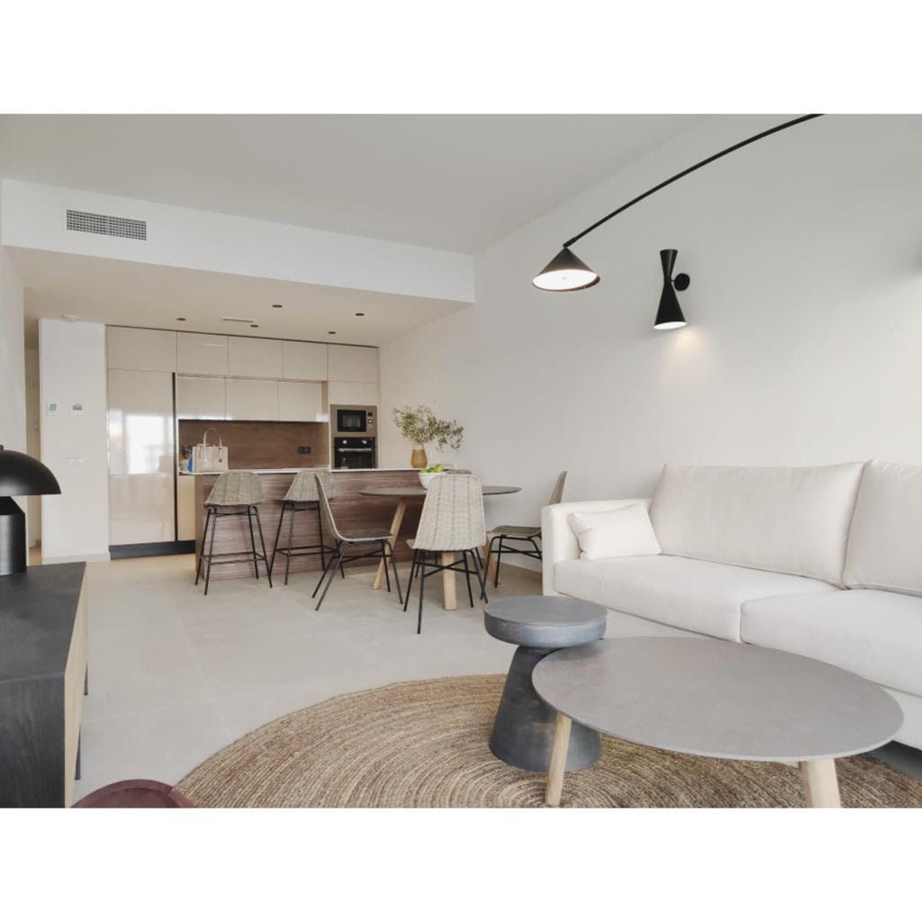 Bright open-concept living room with a white sofa, round coffee tables, and a wooden-kitchen island in the background.