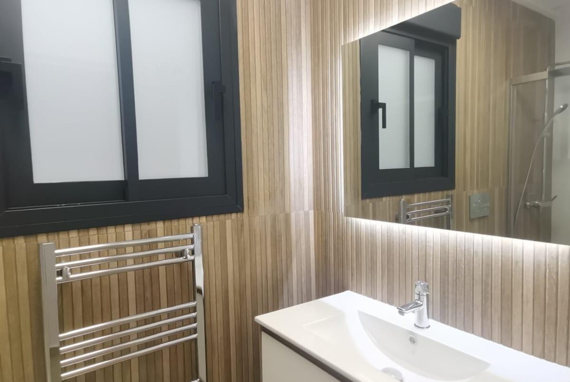 Modern bathroom with vertical wood-paneled walls, a black-framed frosted window, chrome towel warmer, and a white wall-mounted vanity sink.