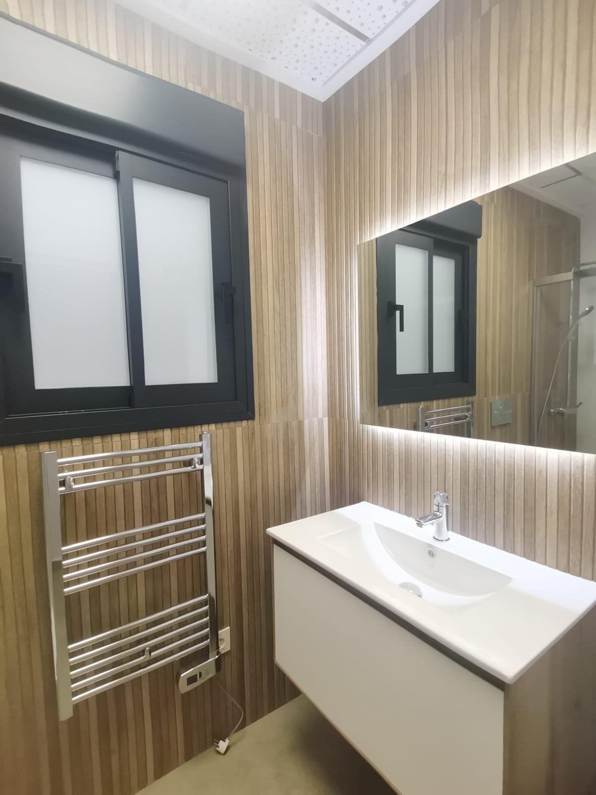 Modern bathroom with vertical wood-paneled walls, a black-framed frosted window, chrome towel warmer, and a white wall-mounted vanity sink.