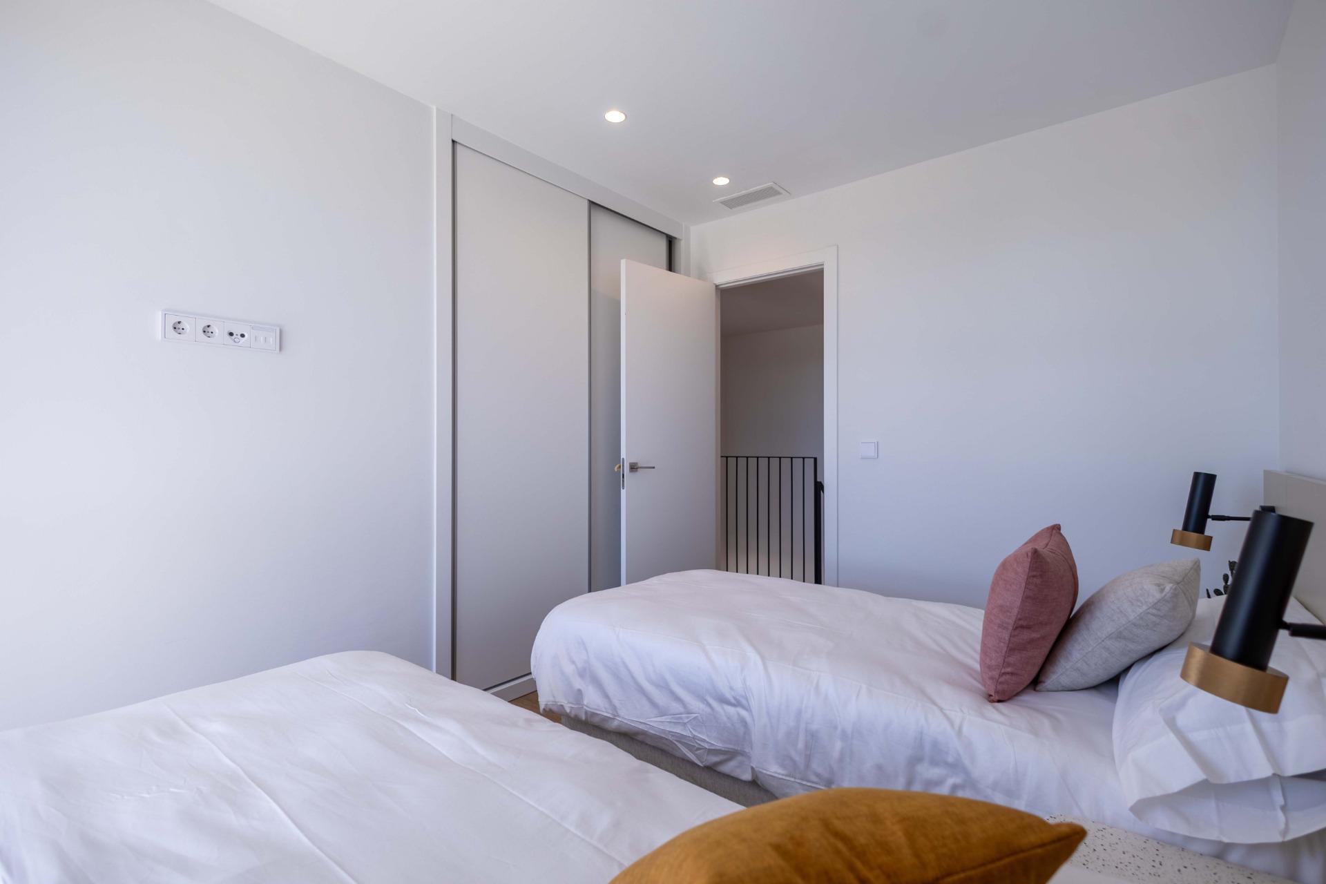Light-filled modern bedroom with two single beds, white linens, and pastel pillows beside a built-in sliding wardrobe.