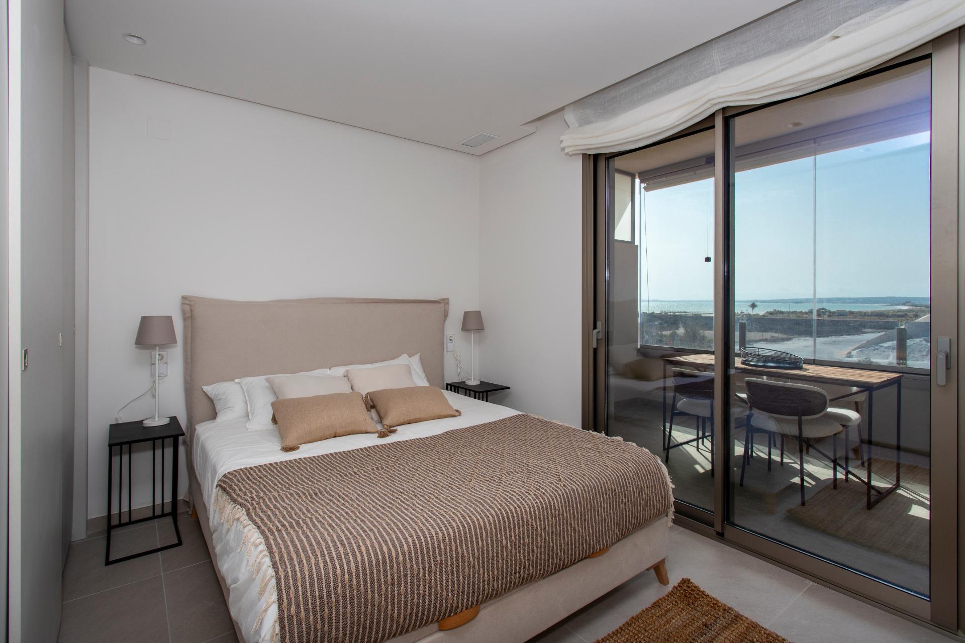 Hotel bedroom with a beige upholstered bed, two nightstands and matching lamps; sliding glass doors open to a balcony with an ocean view.