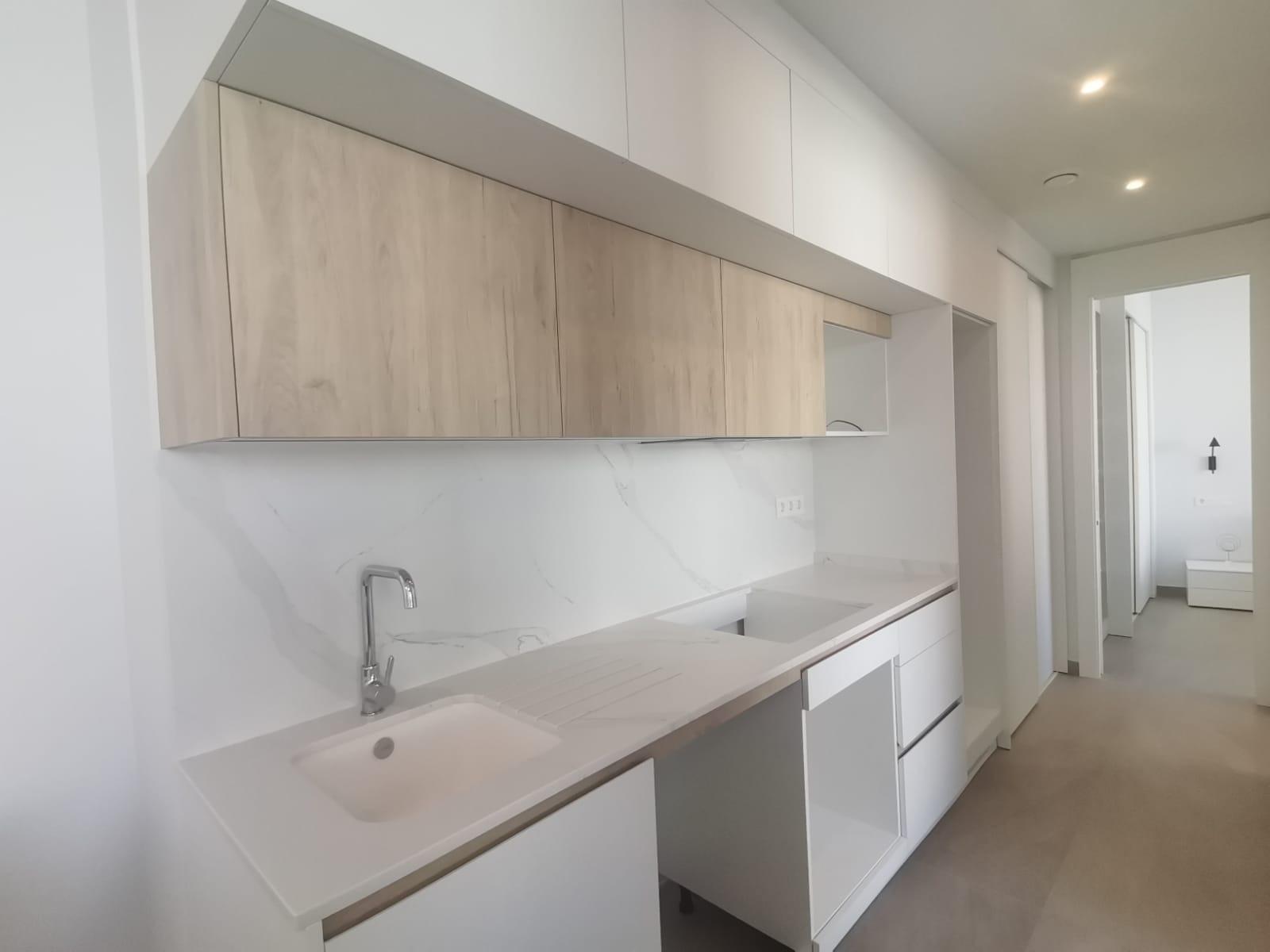 Modern kitchen with white cabinetry, light wood upper cabinets, and a marble backsplash along a long counter and sink area.