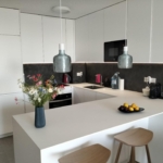 Modern white kitchen with an island, two gray pendant lamps, and a vase of colorful flowers on the counter.