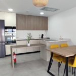 Open-plan kitchen and dining area with a stainless fridge, beige cabinets, and a wooden dining table with yellow chairs.