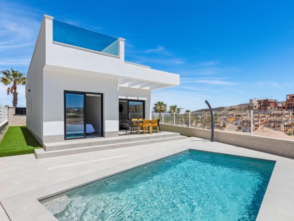 Modern white villa with glass balcony, outdoor dining table, and a rectangular pool under a clear blue sky, palm trees nearby.