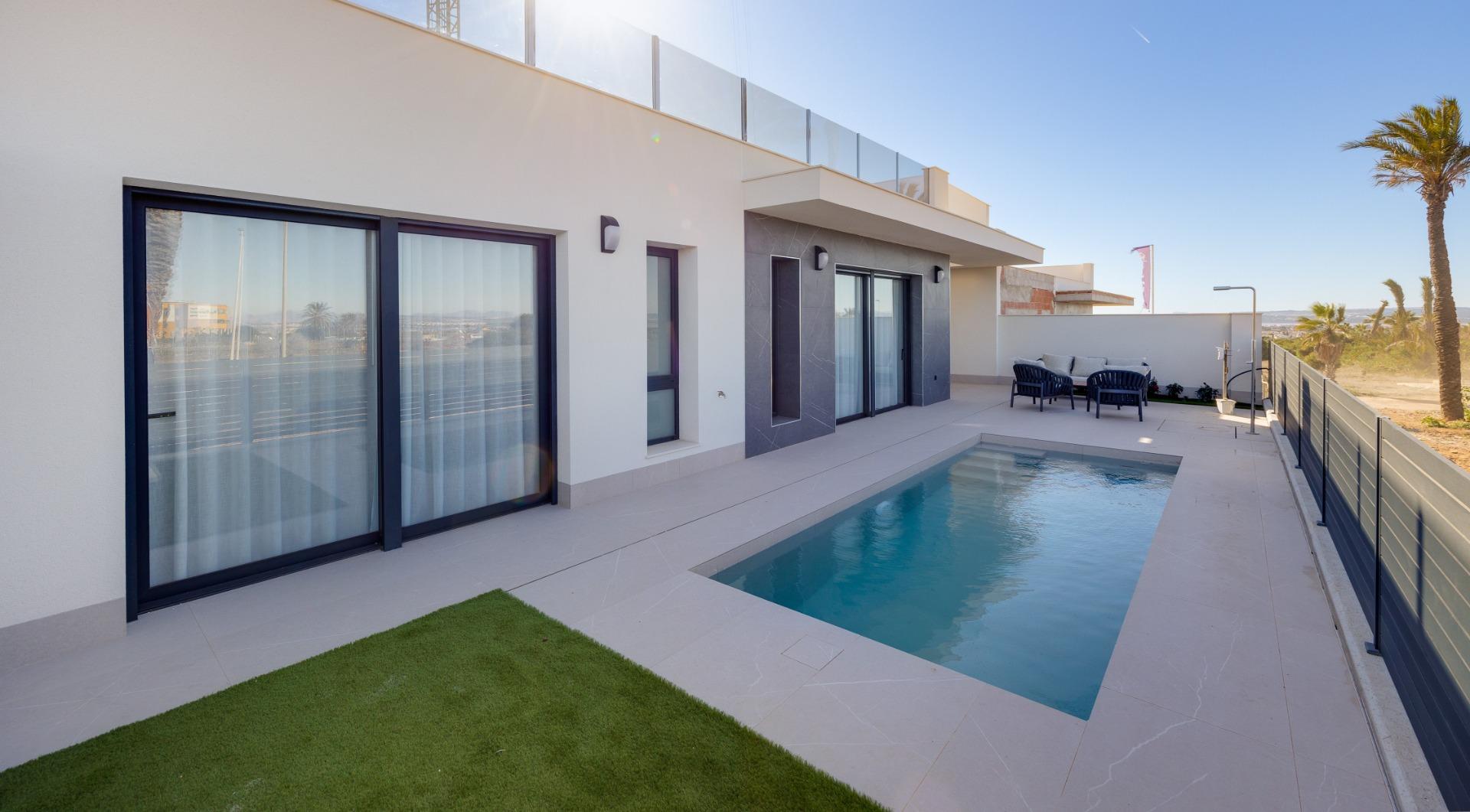 Modern white villa with a rectangular swimming pool and a seating area on a sunny terrace.