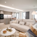 Open-plan living area with a light-gray kitchen, white sofas, and a dining table by large glass doors letting in natural light.