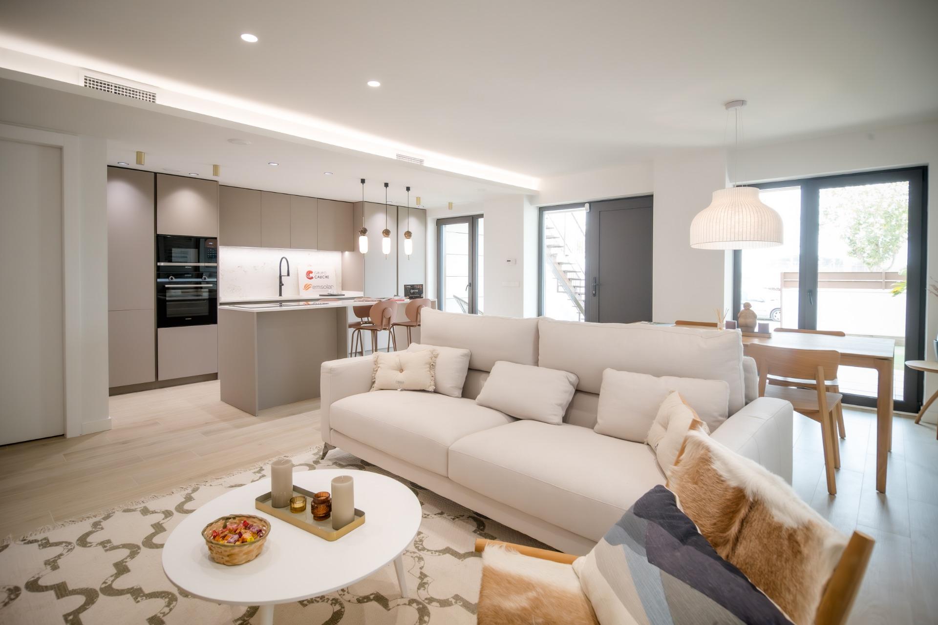 Open-plan living area with a light-gray kitchen, white sofas, and a dining table by large glass doors letting in natural light.