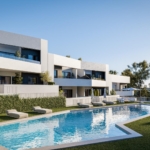 Modern white apartment complex with balconies around a rectangular pool, sun loungers on the lawn, and blue sky above.