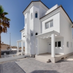 White Mediterranean-style house with arches and palm trees against a clear blue sky, sunny day.