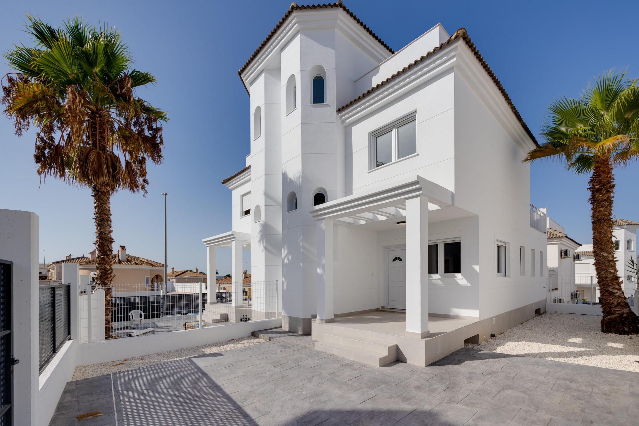White Mediterranean-style house with arches and palm trees against a clear blue sky, sunny day.