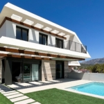 Modern white two-story villa with a rectangular pool and angular overhangs set against a blue sky and mountains.