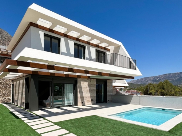 Modern white two-story villa with a rectangular pool and angular overhangs set against a blue sky and mountains.