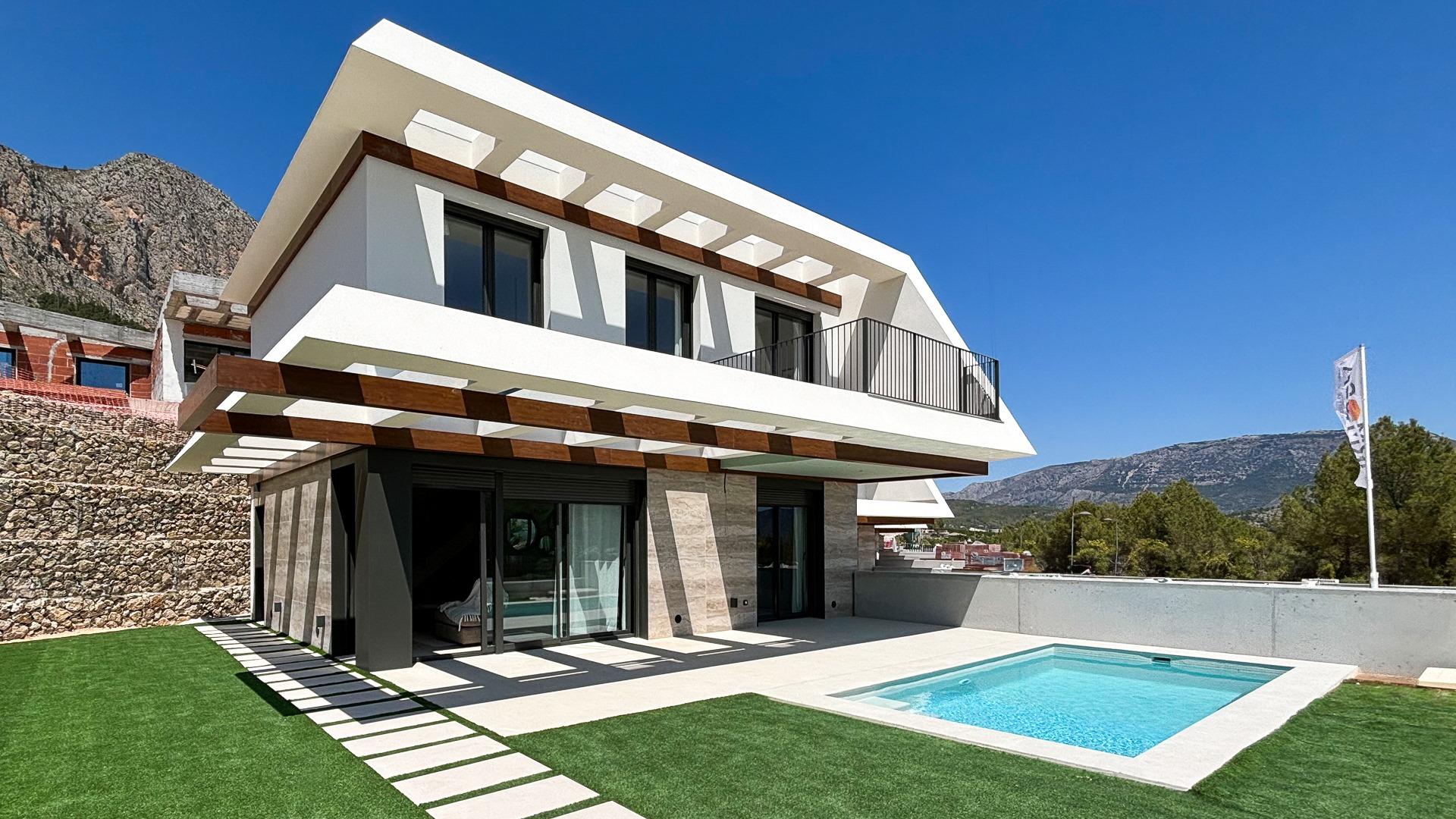 Modern white two-story villa with a rectangular pool and angular overhangs set against a blue sky and mountains.