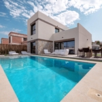 Modern two-story house with a rectangular pool and outdoor seating in a sunny backyard.