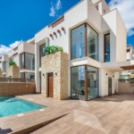 Modern white, two-story villa with large glass windows, stone accents, and a pool on a sunny day.