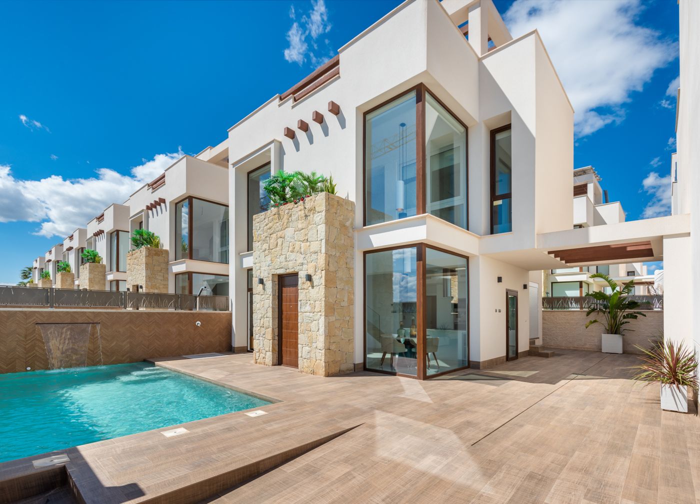 Modern white, two-story villa with large glass windows, stone accents, and a pool on a sunny day.