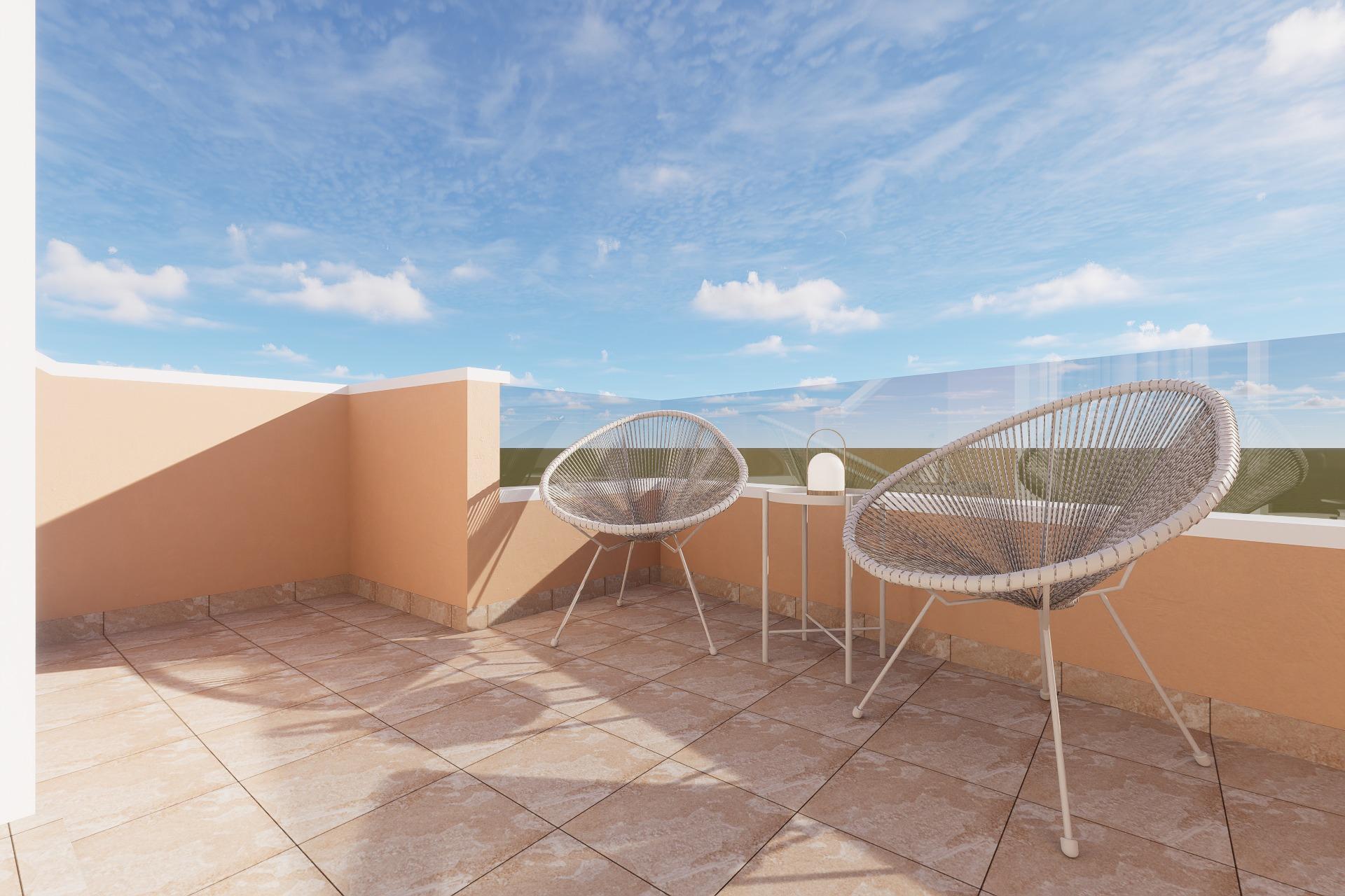 Terrace with peach walls, two woven Acapulco chairs and a small table on tiled floor under a blue sky with clouds.
