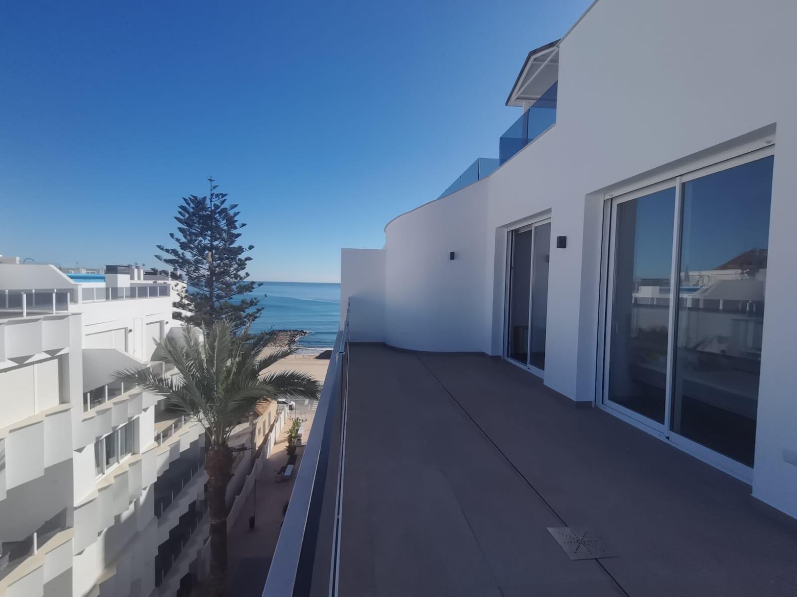 Ocean view from a white modern balcony with sliding glass doors and a blue sky above.