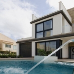 Modern two-story house with a curved stone wall, large windows, and a swimming pool in the foreground.