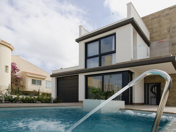 Modern two-story house with a curved stone wall, large windows, and a swimming pool in the foreground.