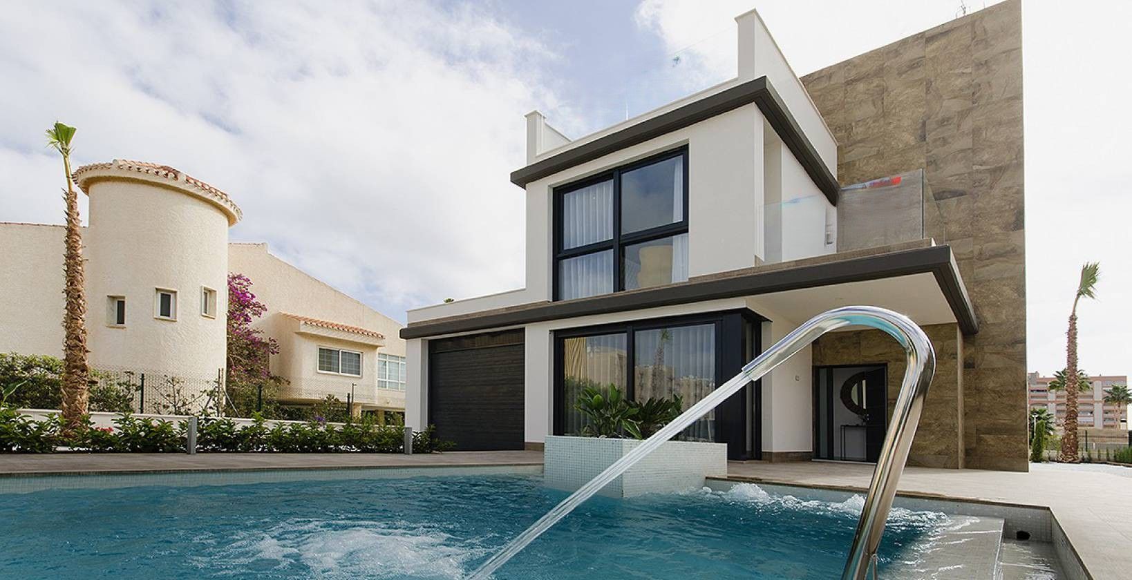 Modern two-story house with a curved stone wall, large windows, and a swimming pool in the foreground.