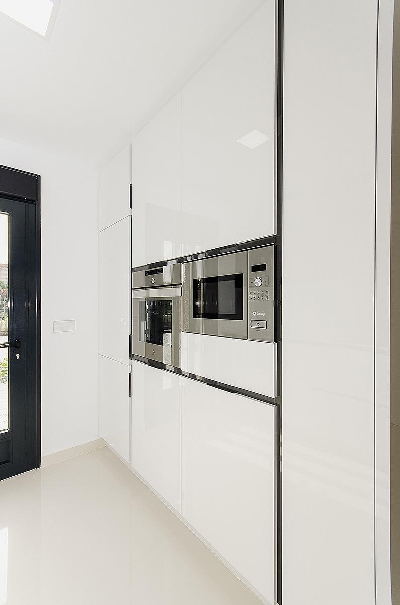 Glossy white kitchen cabinetry with built-in stainless steel oven and microwave, and a dark-framed door on the left.