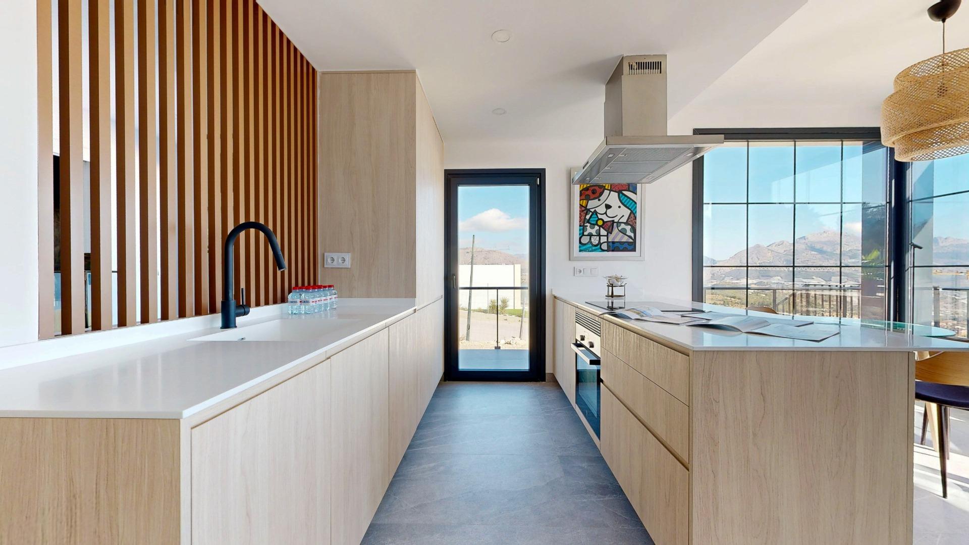 Modern kitchen with light wood cabinetry, a white countertop island, and a black curved faucet; vertical wooden slats wall on left and large windows showing mountains outside.