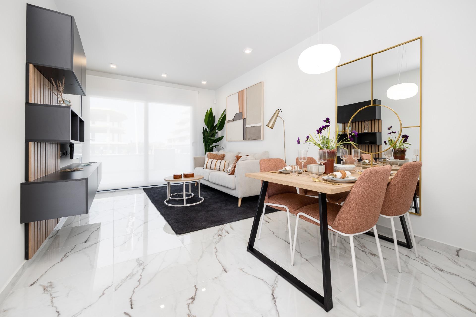 Bright living and dining area with marble floors, a beige sofa, a black wall unit, and a wooden dining table with pink chairs.