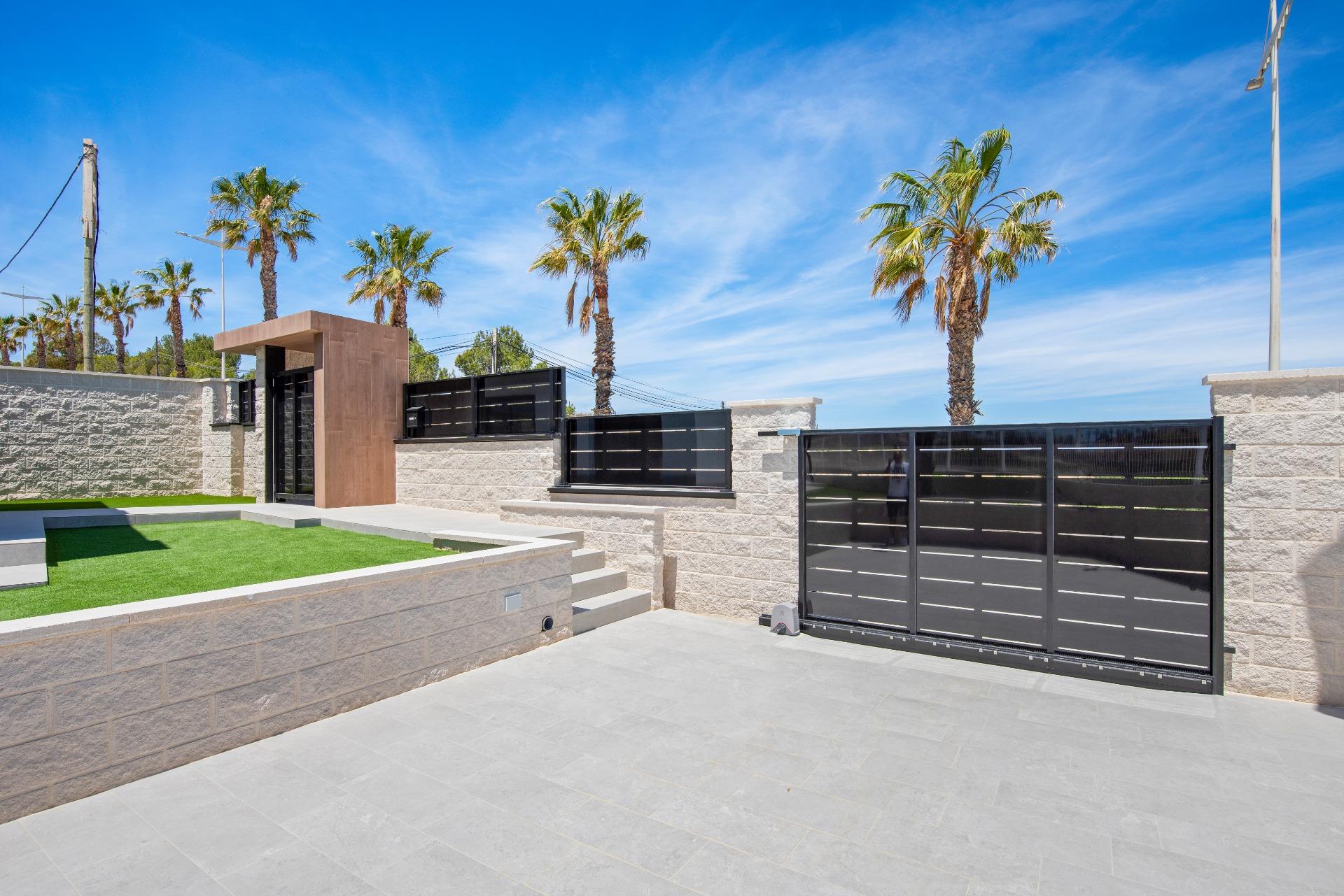 Modern residence exterior with a black metal gate, beige stone walls, and palm trees under a clear blue sky