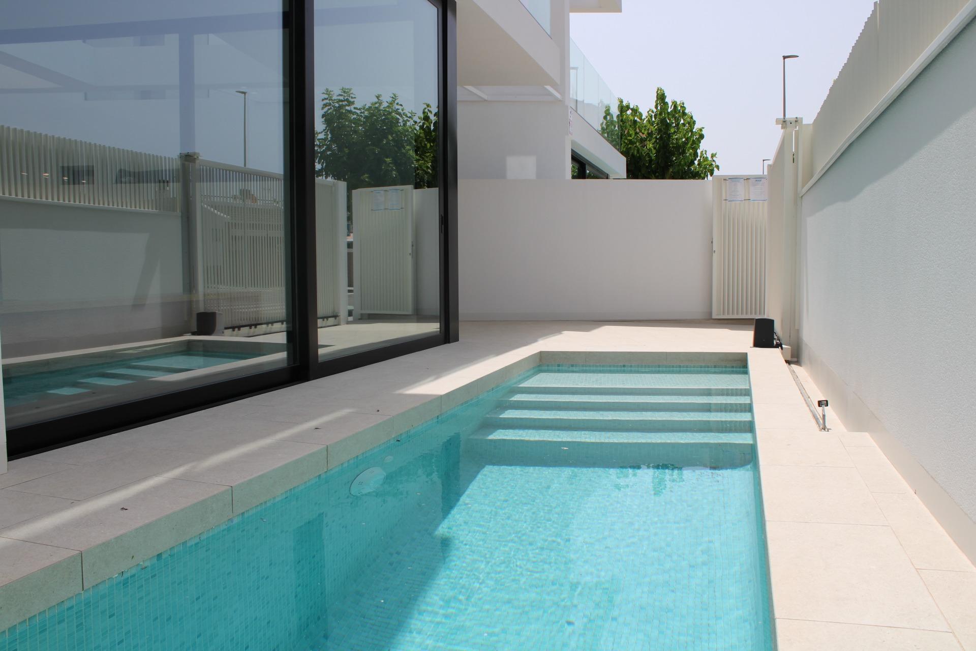 Modern backyard with glass-walled living area, white walls, and a turquoise rectangular pool beside a sleek contemporary home.