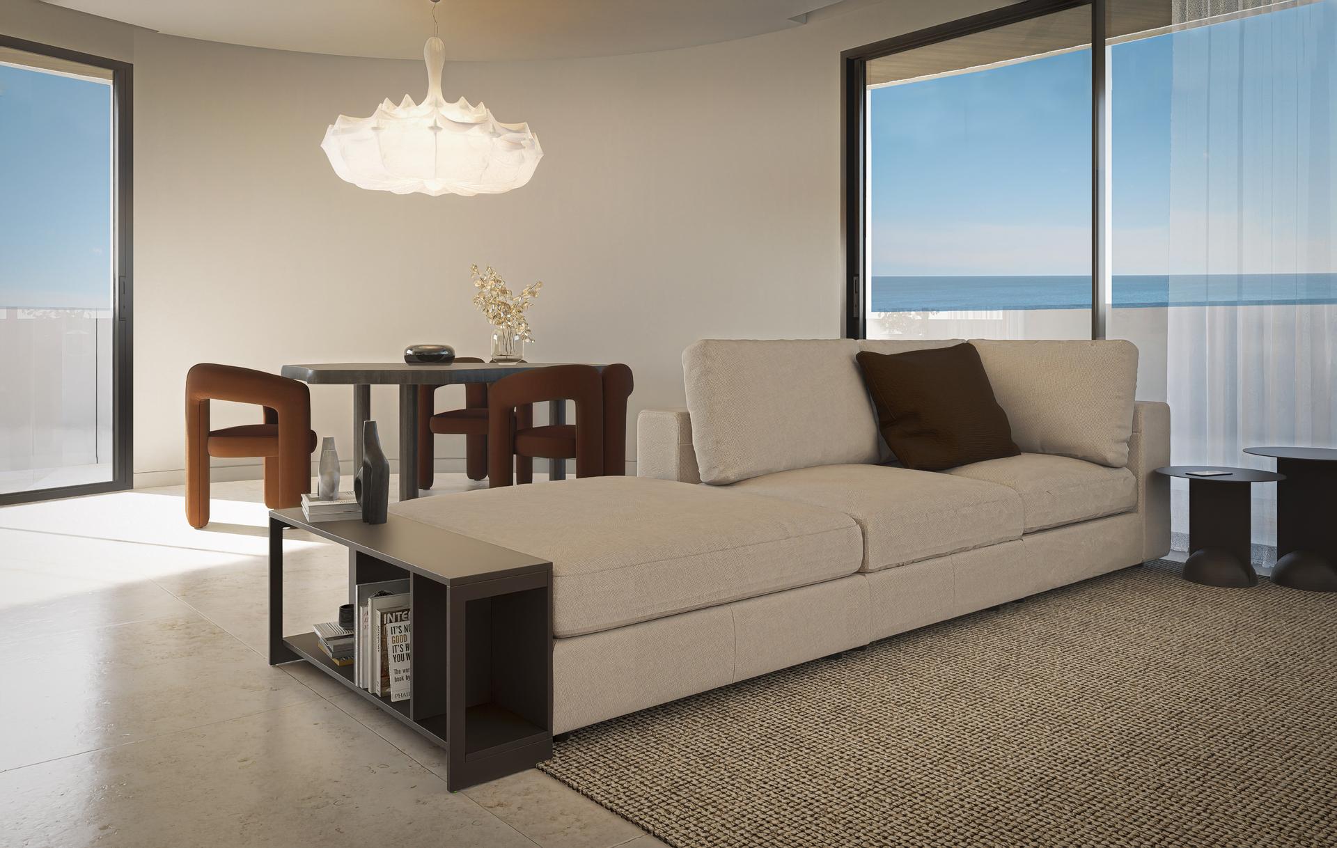 Bright living room with a beige sectional, black coffee table, and round dining table; large windows overlook the ocean.