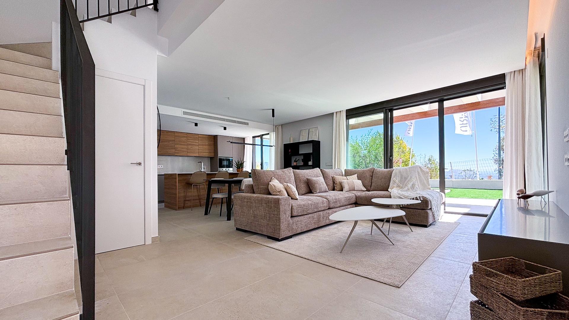 Open-plan living area with a beige sectional sofa, round white coffee tables, and large windows showing a garden outside.
