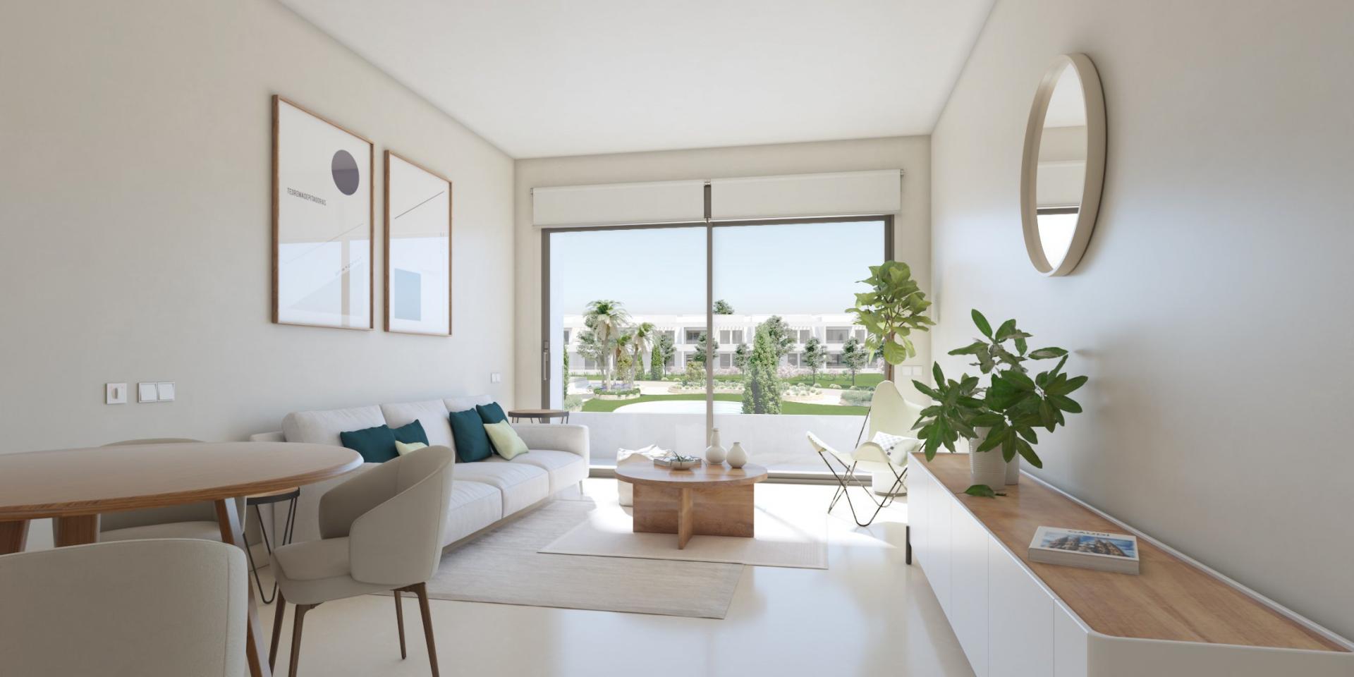 Bright modern living room with a white sofa, teal and pale yellow cushions, a round wooden coffee table, and large glass sliding doors to a sunny courtyard.