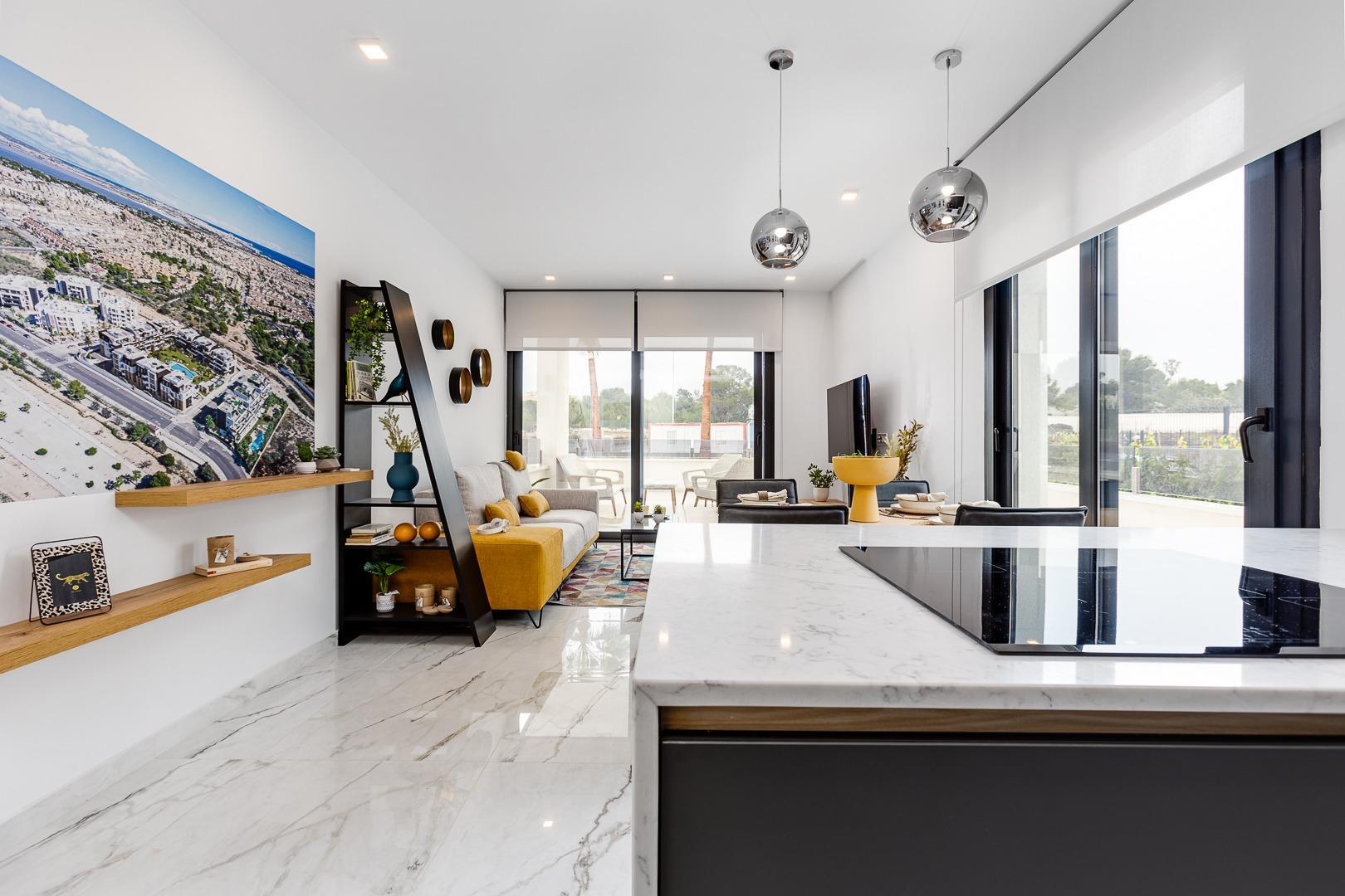 Open-plan living area with a marble kitchen island in the foreground, modern gray sofa, yellow accents, and a large cityscape photo on the wall.
