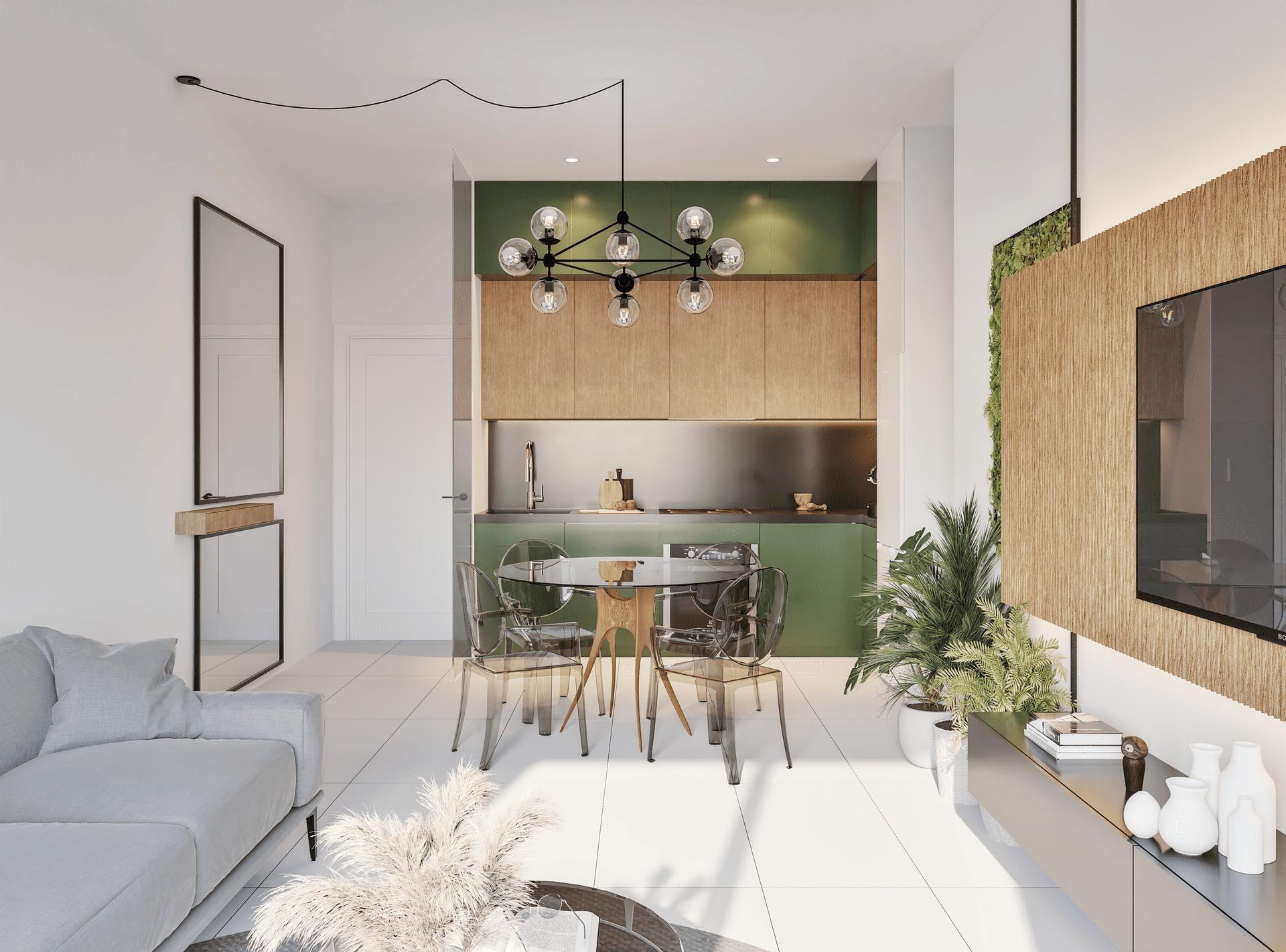 Open-plan living area and kitchen with a round glass dining table, transparent chairs, and a black multi-bulb chandelier over green and wood cabinetry.