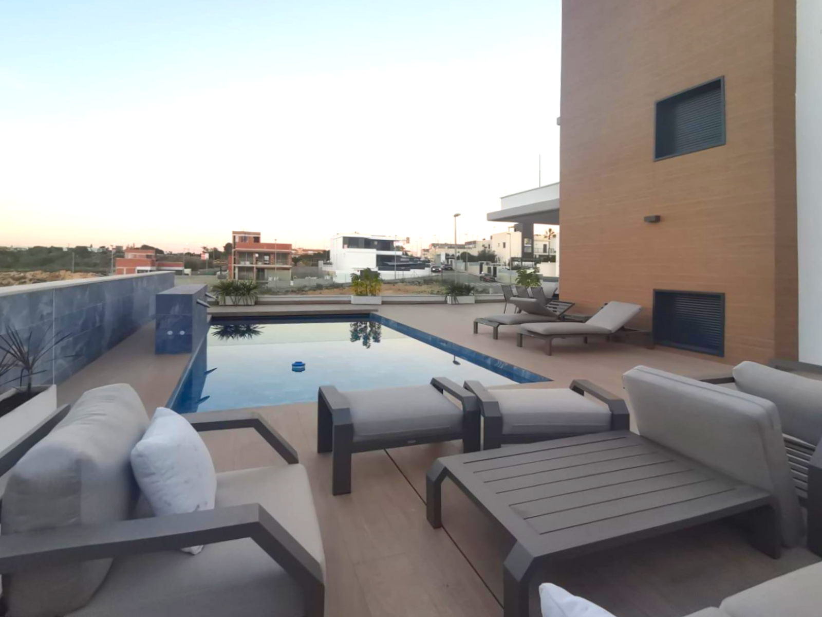 Rooftop pool area with modern gray lounge chairs and a wooden deck overlooking a residential neighborhood.