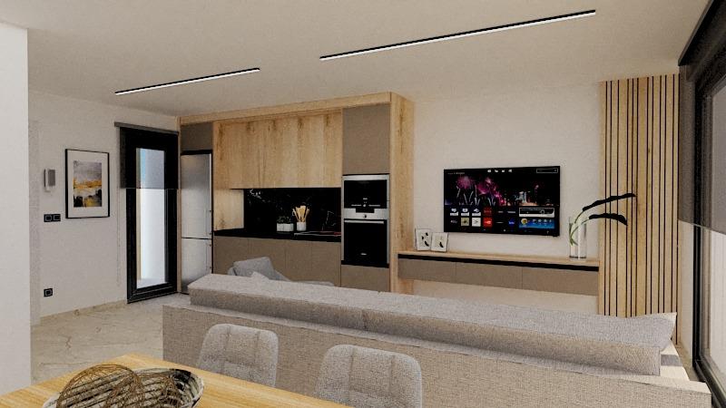 Open-plan living area with a beige L-shaped sofa facing a wall-mounted TV and a light wood kitchen unit along the back wall.